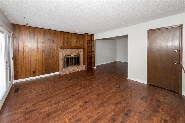 unfurnished living room with visible vents, a textured ceiling, wood finished floors, wooden walls, and a brick fireplace