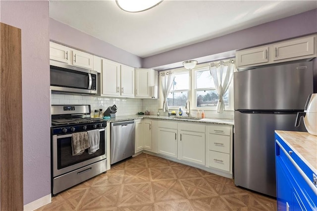 kitchen featuring tasteful backsplash, light floors, white cabinets, stainless steel appliances, and a sink