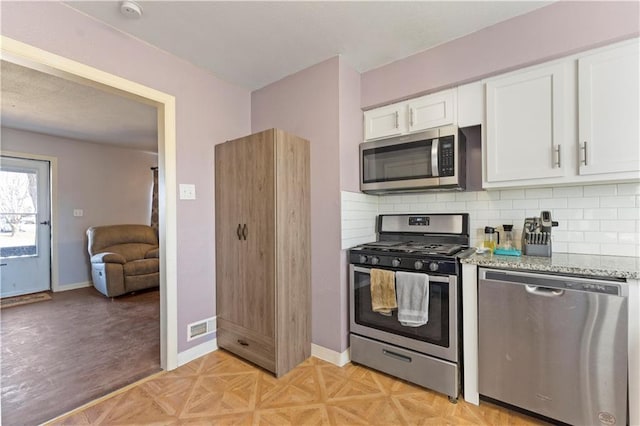 kitchen with light stone counters, backsplash, white cabinetry, appliances with stainless steel finishes, and baseboards