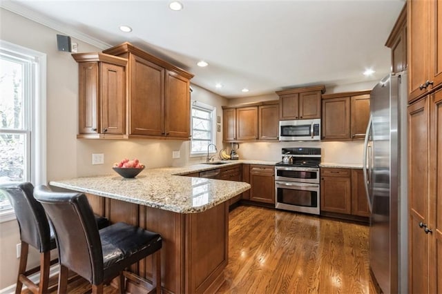 7345 Booth St, Prairie Village, KS 66208 - kitchen with a sink, a peninsula, brown cabinetry, appliances with stainless steel finishes, and dark wood-style flooring