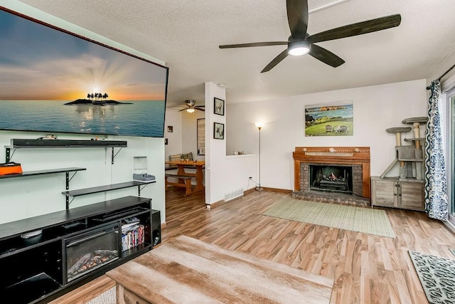 living area with a brick fireplace, visible vents, a textured ceiling, and wood finished floors