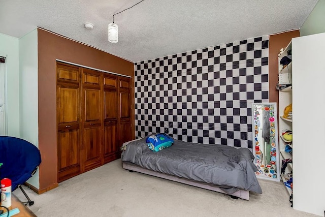 bedroom with carpet floors, an accent wall, a closet, and a textured ceiling