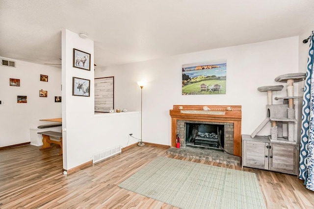 living area with a brick fireplace, wood finished floors, visible vents, and baseboards