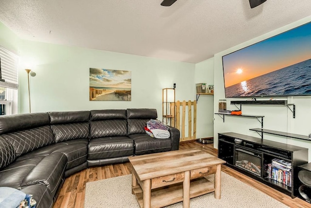 living area featuring ceiling fan, a textured ceiling, wood finished floors, and a glass covered fireplace