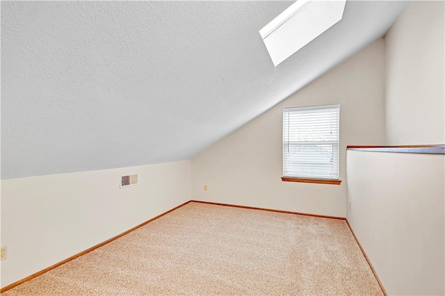 additional living space with visible vents, baseboards, carpet floors, vaulted ceiling with skylight, and a textured ceiling