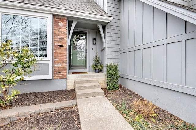 doorway to property with brick siding, board and batten siding, and roof with shingles