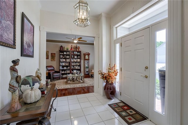 foyer entrance with a wealth of natural light, ceiling fan with notable chandelier, crown molding, and light tile patterned flooring