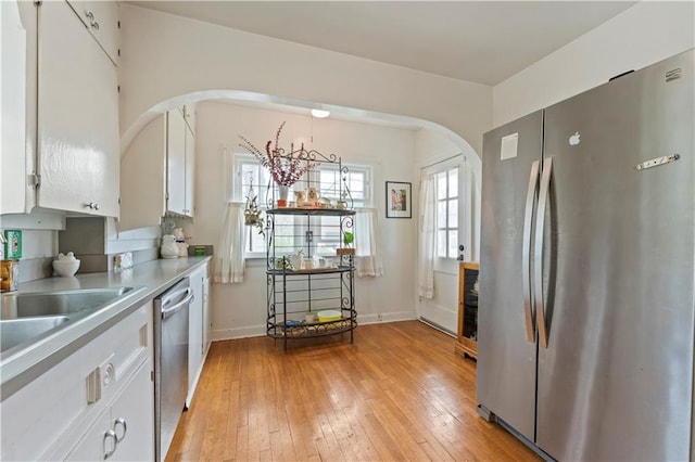 kitchen featuring appliances with stainless steel finishes, arched walkways, white cabinetry, light wood-type flooring, and light countertops