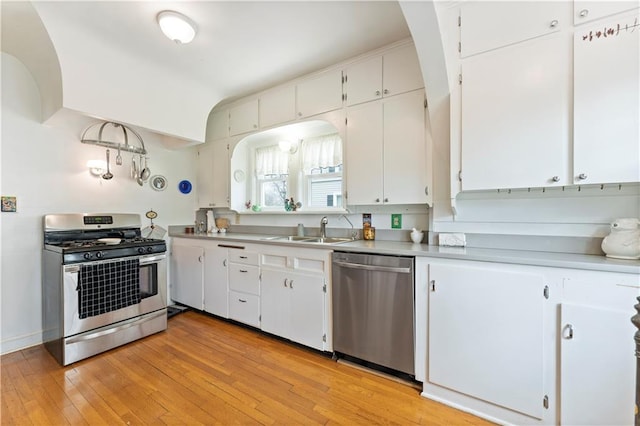 kitchen with stainless steel appliances, a sink, white cabinetry, and light wood-type flooring