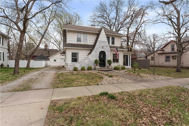 view of front of house featuring fence, a chimney, dirt driveway, and stone siding