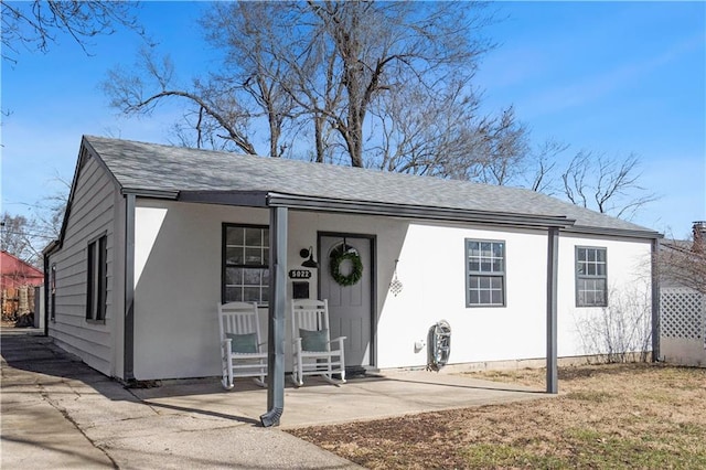 view of front facade featuring a shingled roof, a porch, and stucco siding