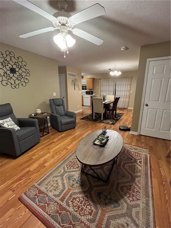 living area with baseboards, visible vents, light wood-style flooring, a textured ceiling, and ceiling fan with notable chandelier