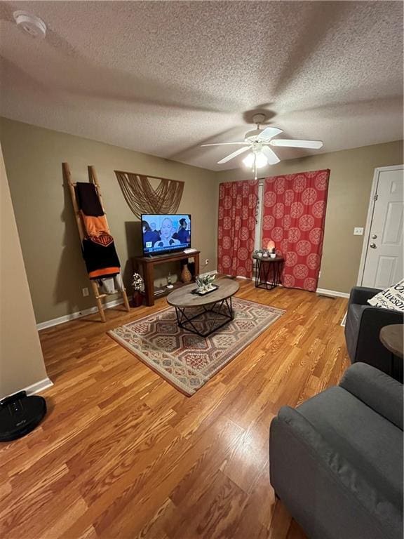 living area with a textured ceiling, wood finished floors, a ceiling fan, and baseboards