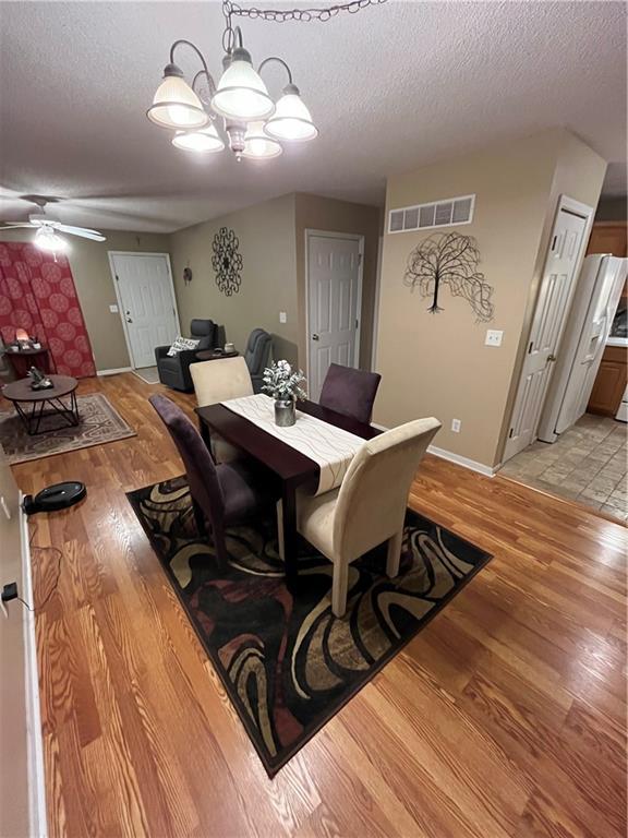 dining room with baseboards, visible vents, light wood-style flooring, a textured ceiling, and ceiling fan with notable chandelier