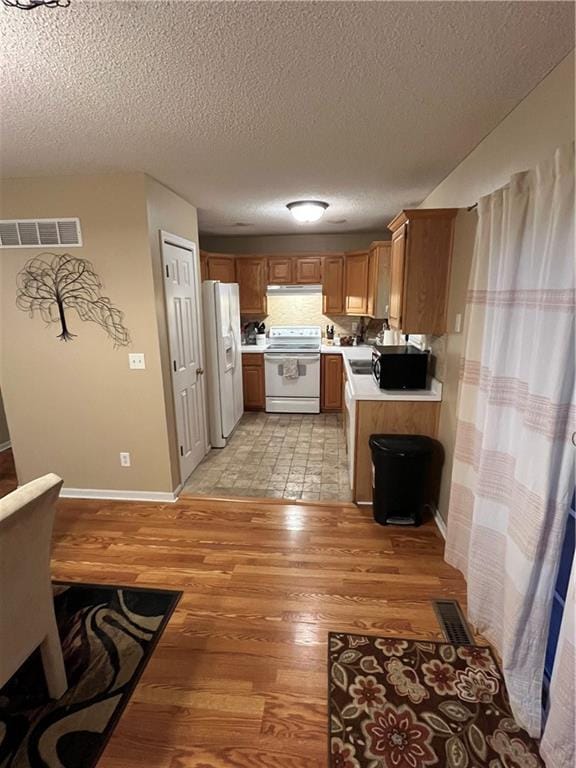 kitchen featuring under cabinet range hood, white appliances, visible vents, light countertops, and light wood finished floors