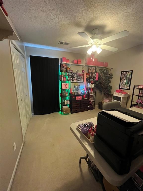 interior space with a textured ceiling, carpet floors, visible vents, and a ceiling fan