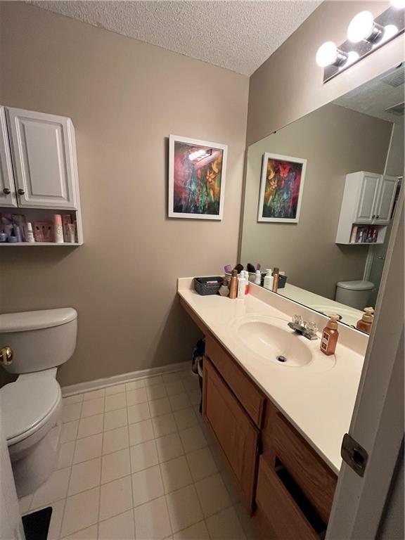 bathroom featuring a textured ceiling, toilet, vanity, baseboards, and tile patterned floors