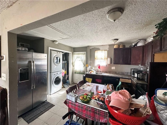 kitchen with stainless steel refrigerator with ice dispenser, light tile patterned floors, stacked washer / dryer, dark brown cabinetry, and a textured ceiling