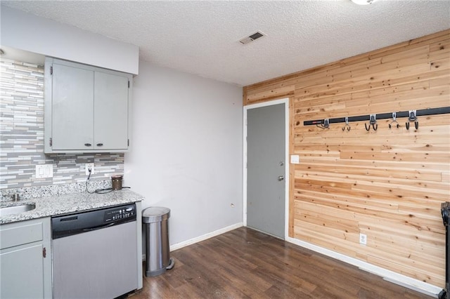 kitchen with a textured ceiling, dark wood-type flooring, wood walls, visible vents, and stainless steel dishwasher