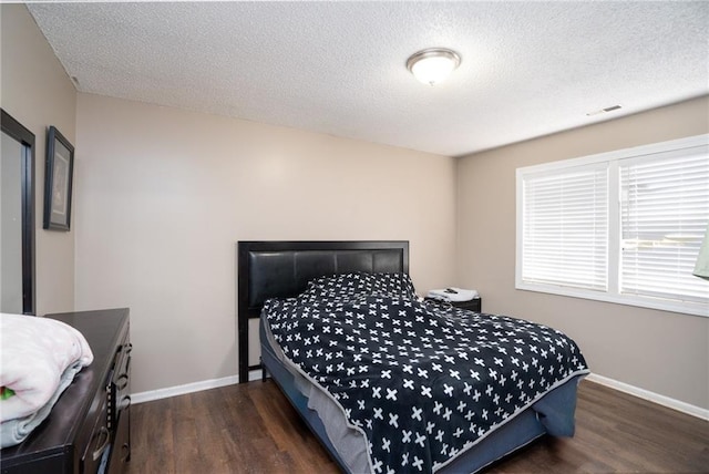 bedroom with visible vents, dark wood finished floors, a textured ceiling, and baseboards