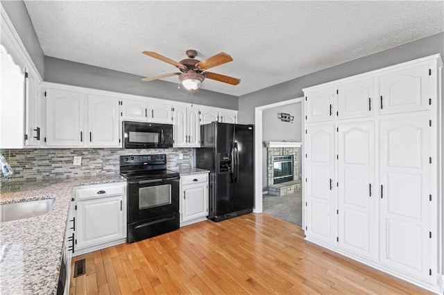 kitchen with white cabinets, a sink, light wood finished floors, and black appliances