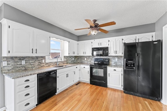 kitchen with black appliances, a sink, white cabinetry, and light stone countertops