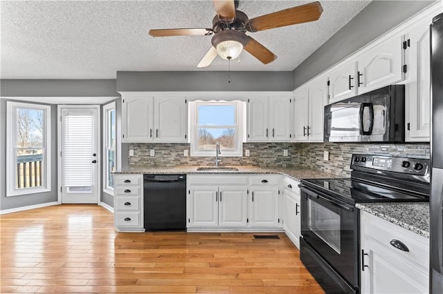 kitchen with light stone counters, white cabinetry, a sink, and black appliances