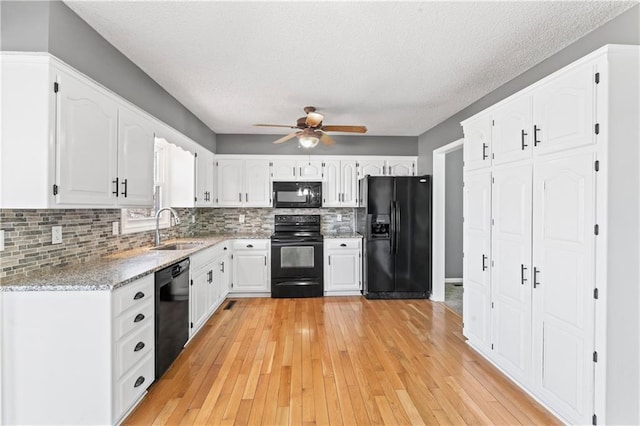 kitchen featuring a sink, white cabinetry, light wood-type flooring, black appliances, and tasteful backsplash