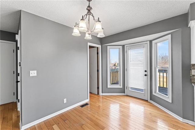 unfurnished dining area with light wood-style floors, baseboards, visible vents, and a textured ceiling