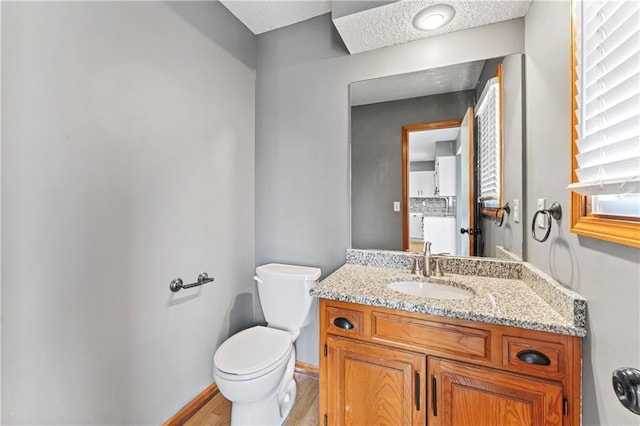 bathroom featuring toilet, baseboards, wood finished floors, and vanity