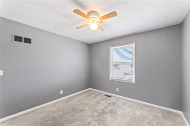 carpeted spare room with a ceiling fan, visible vents, and baseboards