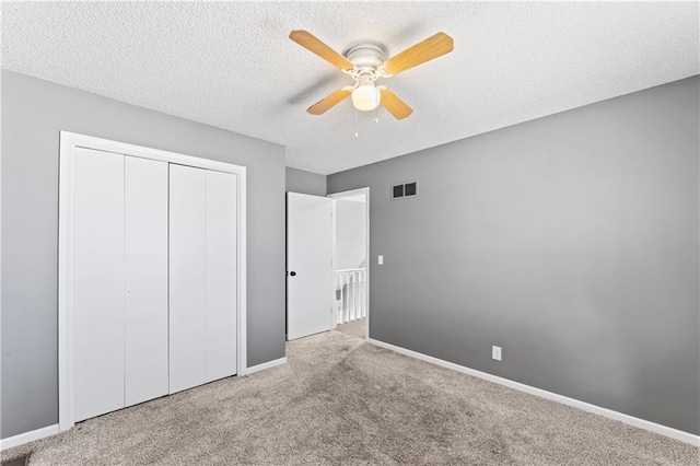 unfurnished bedroom with a textured ceiling, light colored carpet, visible vents, baseboards, and a closet