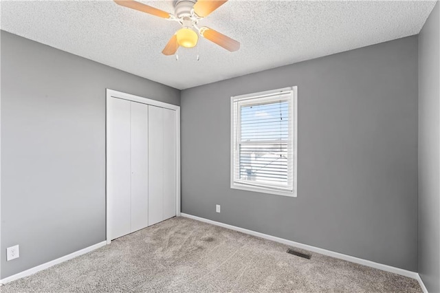 unfurnished bedroom featuring light carpet, baseboards, visible vents, a textured ceiling, and a closet