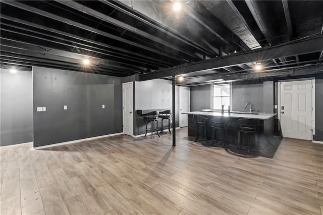 basement featuring light wood finished floors, indoor wet bar, and baseboards