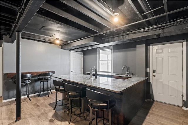 interior space with a peninsula, light wood finished floors, stone counters, and a sink