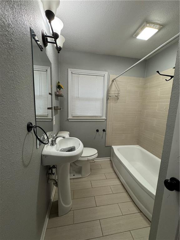 1403 E Mechanic St, Harrisonville, MO 64701 - full bath with shower / bathtub combination, toilet, baseboards, wood tiled floor, and a textured ceiling