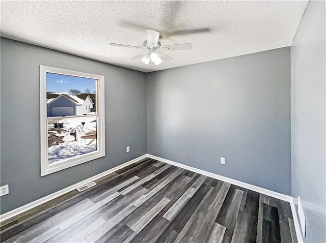 empty room with a textured ceiling, dark wood-type flooring, visible vents, a ceiling fan, and baseboards