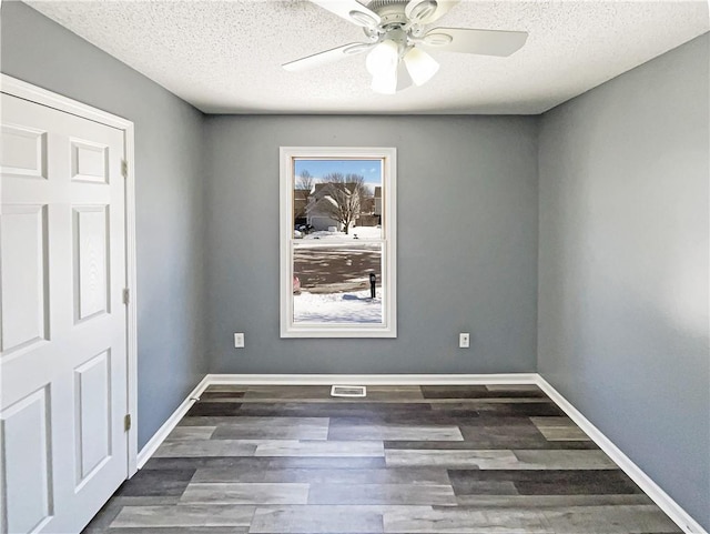 spare room with visible vents, baseboards, a ceiling fan, dark wood-type flooring, and a textured ceiling