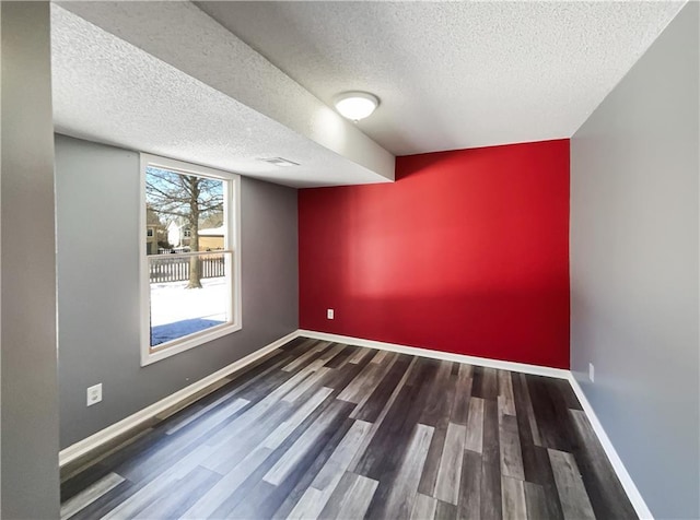 empty room with a textured ceiling, an accent wall, baseboards, and dark wood-type flooring