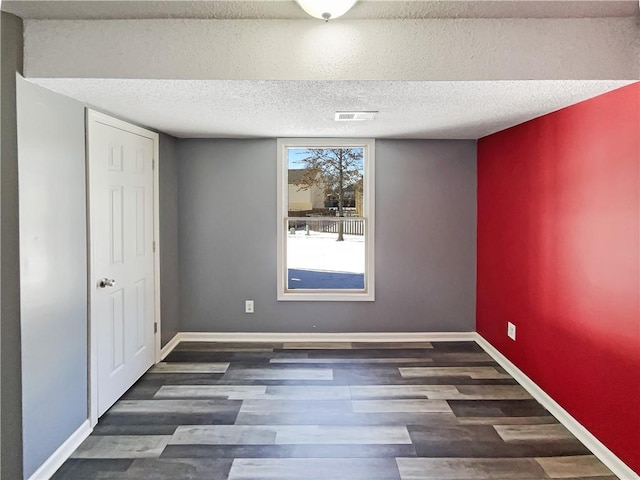 spare room with dark wood-style flooring, visible vents, a textured ceiling, and baseboards