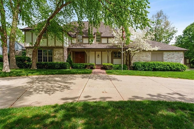english style home featuring brick siding, a front lawn, stucco siding, and covered porch