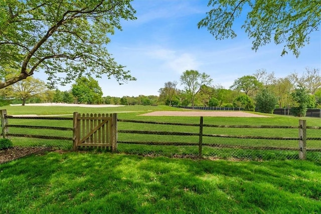 view of gate with fence, a yard, and a rural view