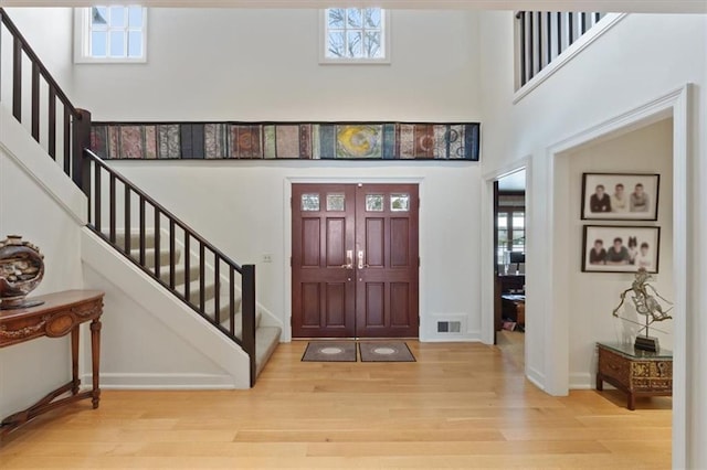 foyer with stairs, visible vents, a healthy amount of sunlight, and wood finished floors