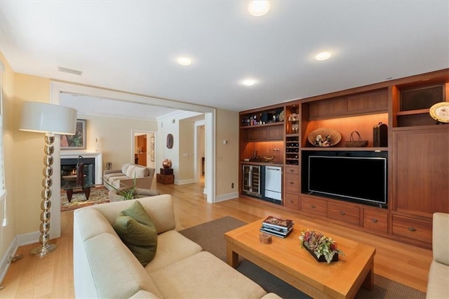 living room with a wood stove, beverage cooler, baseboards, a dry bar, and light wood-style flooring