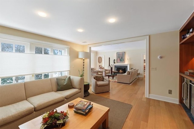 living room with baseboards, a glass covered fireplace, and light wood finished floors