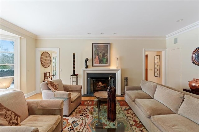 living room featuring a glass covered fireplace, baseboards, ornamental molding, and light wood-style flooring