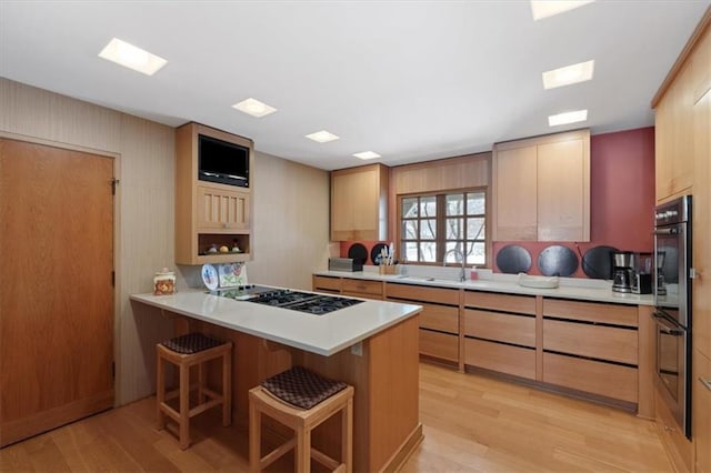 kitchen featuring light wood finished floors, a breakfast bar area, light countertops, black gas cooktop, and a peninsula