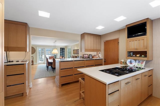 kitchen with light brown cabinetry, black gas cooktop, light countertops, light wood finished floors, and a peninsula
