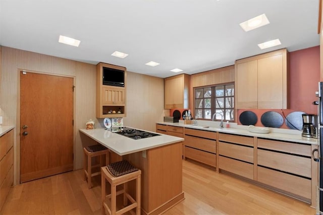 kitchen featuring a breakfast bar area, black gas cooktop, a sink, light countertops, and light wood finished floors