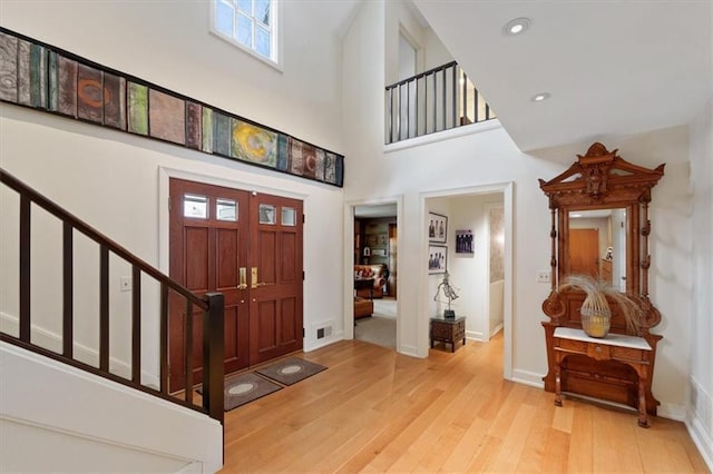 foyer entrance featuring a high ceiling, baseboards, light wood-type flooring, visible vents, and stairway
